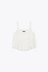 Top blanco de lino con escote recto y tirantes. Presenta detalle de bordados calados y aberturas laterales con lazadas.