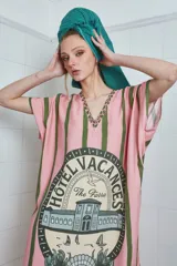 Túnica larga celeste con rayas verticales marrones y estampado central con el logo de un hotel. Tiene cuello en V con detalle de puntilla y tajos laterales.