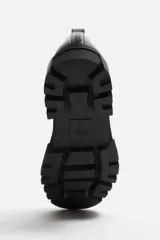 Zapato de vestir tipo blucher color negro, con detalle de bordón, tirador trasero y horma redonda. Suela con volumen y diseño irregular.