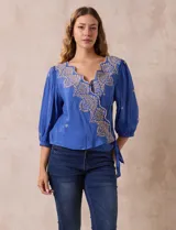 Blusa azul con bordados color crema, escote en V cruzado, mangas 3/4 abullonadas y nudo en el ruedo.