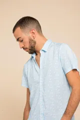 Camisa celeste con estampado floral blanco, de manga corta y corte clásico. Cierre frontal con botones.