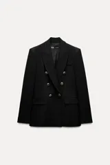 Blazer negra de corte entallado, con cuello y solapa, mangas largas con hombreras marcadas, bolsillos frontales con solapa y cierre cruzado con botones dorados.