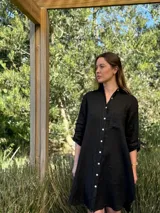 Vestido camisero blanco de lino, con cuello camisero, manga larga con botón para recoger, cierre frontal con botones de nácar, bolsillo en el pecho y diseño asimétrico más largo en la parte trasera.