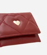 Billetera pequeña tipo sobre color bordó, confeccionada en poliuretano con textura capitoneada y aplique de corazón dorado.