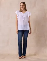 Blusa blanca de gasa con broderie, cuello a la base, escote en V y lazo de ajuste. Delantera broderie con corte y frunces. Manga corta volado de broderie. Espalda con corte y frunces.