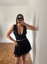 Top corto negro con lunares blancos, escote en V, mangas cortas con lazos en los hombros y corte ajustado.