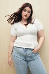 Top blanco con textura tramada, escote en V con leve frunce central, mangas cortas con elástico y volado sutil en el ruedo. Tejido con elasticidad.