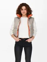 Chaleco acolchado color beige con cuello alto y cierre frontal con cremallera. El interior es color naranja.