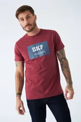 Remera de algodón color bordó con estampado rectangular azul con letras blancas en el frente.