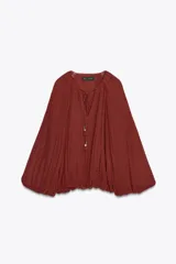 Blusa color ladrillo con textura de lunares, cuello redondo con cordón ajustable con borlas, manga larga abullonada con puños elásticos y ruedo elástico.