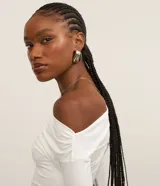 Blusa corta color blanco, con escote canoa que deja un hombro al descubierto y mangas largas.
