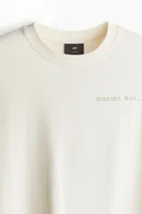 Remera color crema de corte holgado con cuello redondo y estampado pequeño en el pecho.