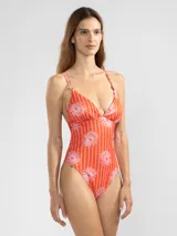 Traje de baño enterizo de lycra color naranja con rayas verticales blancas y estampado de flores rosas. Tiene escote en V, breteles finos y charms florales en los tirantes.