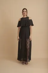 Vestido largo negro con transparencias y encaje. Tiene escote redondo, corte a la cintura y falda larga con paneles de encaje floral. El cuerpo superior es de gasa con hombros descubiertos y volado.