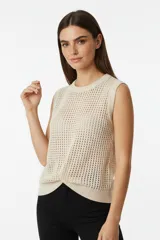 Chaleco color crema de punto calado, sin mangas y con terminación cruzada en el frente.