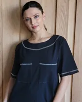 Vestido midi negro con cuello redondo y mangas cortas. Presenta dos bolsillos cuadrados en el pecho y ribetes blancos en cuello, mangas, bolsillos y ruedo.
