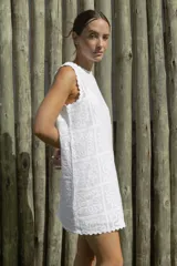 Vestido corto blanco con estampado de flores y diseño geométrico, sin mangas y con terminaciones onduladas en cuello y ruedo.