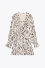 Vestido corto de Zara Woman Collection confeccionado en hilatura de algodón. Presenta escote pico ajustable con lazadas, mangas largas con elástico y volante en los puños, y bajo evasé con abertura.