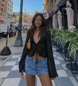 Top negro de manga larga, ligeramente traslúcido, con escote pronunciado en V y detalle de volados en el borde del escote. Se anuda en el centro del busto.