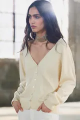 Cárdigan color crema de punto fino con escote en pico, cierre frontal con botones y manga larga.