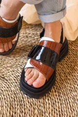 Sandalias marrones con tiras anchas de cuero texturizado y gamuza, suela track negra y hebilla ajustable en el tobillo.