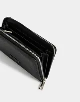 Billetera negra rectangular con cierre circundante y tag metálico con logo.