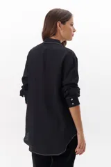 Camisa negra de manga larga con cuello clásico y cierre frontal con botones. Presenta costuras decorativas en color blanco.