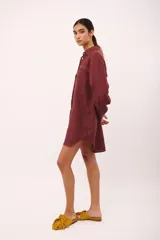 Vestido camisero corto color borgoña de lino italiano, con cuello camisero, manga larga, cierre frontal con botones y dos bolsillos de parche en el pecho con bordado de cerezas.