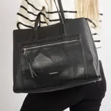Cartera tipo tote bag de cuero sintético color negro, con doble asa de hombro, bolsillo frontal con cierre y logo metálico de la marca.
