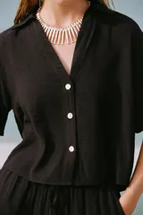 Camisa negra de manga corta con cuello solapa y escote pico. Detalle de nido de abeja en la espalda y cierre frontal con botones.