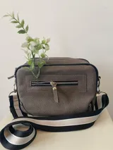 Bandolera gris con correa de tela a rayas blancas, negras y grises.