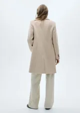 Abrigo de paño color beige, con cuello de solapa, doble botonadura y bolsillos con solapa.