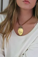 Collar con dije dorado texturizado en forma de lágrima y cordón doble de cuero marrón.