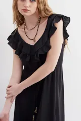 Vestido largo negro sin mangas, con escote redondo, espalda baja y volados en el escote. Ajuste en la cintura con cordón y terminaciones metálicas.