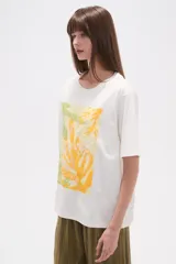 Remera blanca de manga corta y corte holgado, con un estampado central que simula una mano haciendo el signo de la paz, con detalles bordados y lentejuelas en tonos amarillo, verde claro y blanco.