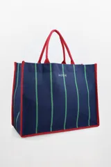Bolso tote azul marino con rayas verticales verdes y ribetes rojos. Tiene asas de mano rojas y un logo dorado estampado en el centro. Incluye un pouch interno.