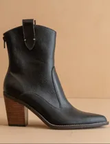 Bota corta de cuero negro con puntera fina, caña media y cierre lateral. Tiene un tirador trasero y un tacón de madera.