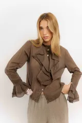 Camisa celeste de algodón con cuello alto y volados frontales. Mangas largas con puños fruncidos.