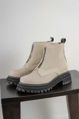 Botas cortas color beige con cierre frontal de cremallera, suela track negra y tirador trasero.