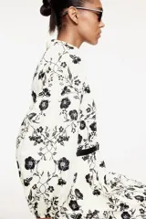 Vestido corto de algodón color crema con estampado floral negro, cuello mao, escote en V, mangas globo con puños elásticos, falda balloon y cinturón extraíble con hebilla ovalada.