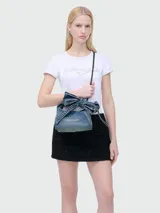 Bandolera mini tipo saco de denim celeste con lazo decorativo y correa fina negra.