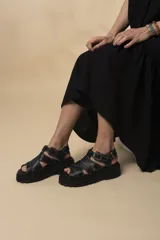 Sandalias negras de cuero con plataforma y tiras entrecruzadas con costuras blancas.