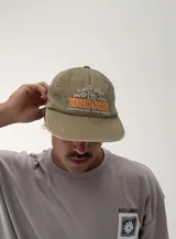 Gorro tipo gorra de béisbol color beige, con visera curva y estampado frontal con la palabra "HUDSUN" en naranja y blanco, y texto "It all started here 1975 sunset flower".