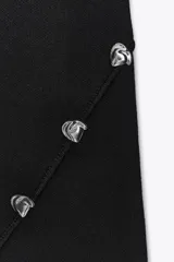 Vestido corto negro de punto, con cuello redondo y sin mangas. Tiene una abertura en el ruedo y detalle de botones metálicos irregulares cruzados en el lateral.