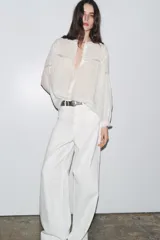 Camisa blanca de ramio con cuello redondo, mangas largas con puños elásticos y cierre frontal con botones.