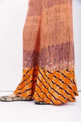 Pantalón amplio de viscosa y modal con cintura elastizada. Presenta un estampado batik en tonos naranja, terracota y morado, con textura plisada y apliques de lentejuelas circulares plateadas.
