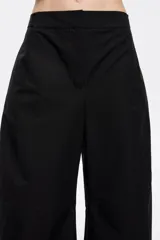 Pantalón negro de tejido técnico con corte barrel, cierre de corchete oculto y cremallera, trabillas ajustables en cintura y bajo, bolsillos delanteros en costuras y bolsillos con vivo en la parte posterior.