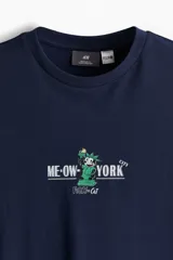 Remera azul marino de algodón con cuello redondo y estampado frontal con un gato disfrazado de Estatua de la Libertad y la frase "Me-OW-York City".
