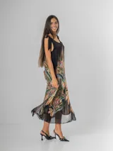 Vestido midi negro con estampado tropical de hojas y flores en tonos tierra, naranja y verde. Es de tirantes anchos con nudo regulable en el hombro y tiene aberturas laterales.