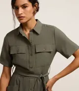 Vestido midi color verde militar, estilo camisero, con cuello clásico, mangas cortas, abotonadura frontal completa, bolsillos utilitarios en el pecho, lazo en la cintura y falda acampanada.
